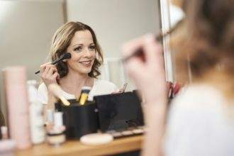 Portrait of smiling woman applying make up at the mirror